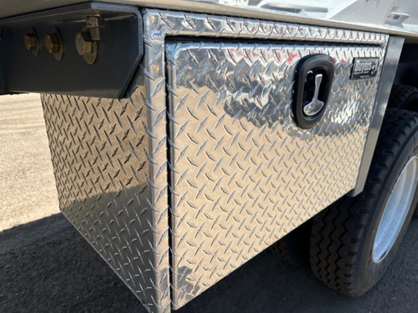 Diamond plate aluminum toolbox on side of trailer with tie-down rings and wheel in background.