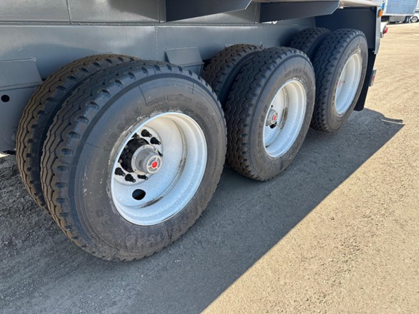 Trailer wheel axles showing three tandem tires with rims and lug nuts on a vacuum water tank trailer.