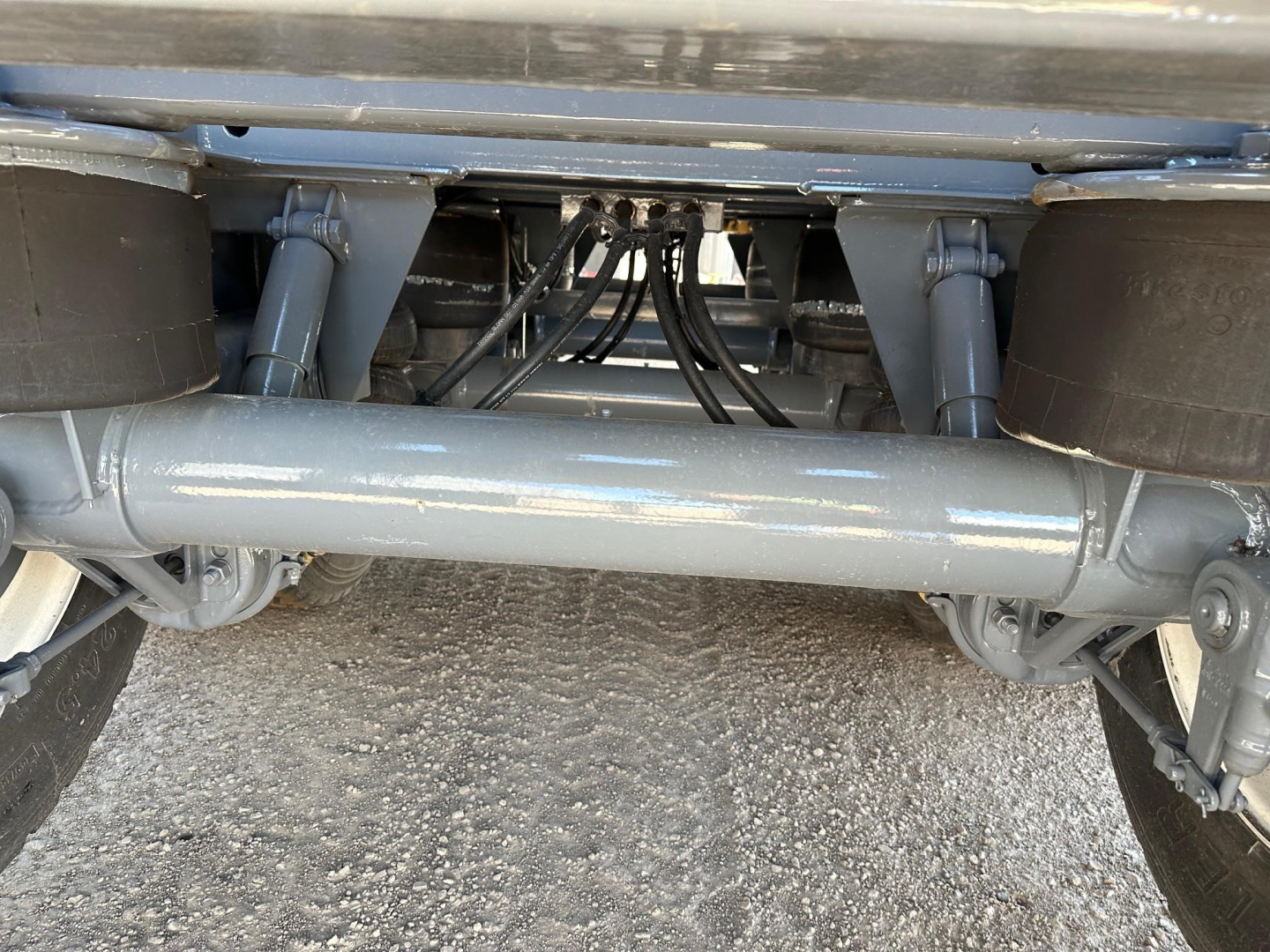 Trailer undercarriage showing solid axle and suspension with hydraulic lines and frame beams.