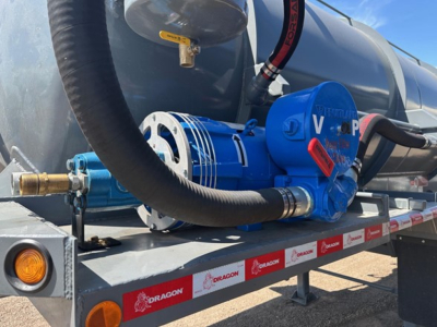 Blue vacuum pump mounted on a metal trailer with hoses and a large tank in background.