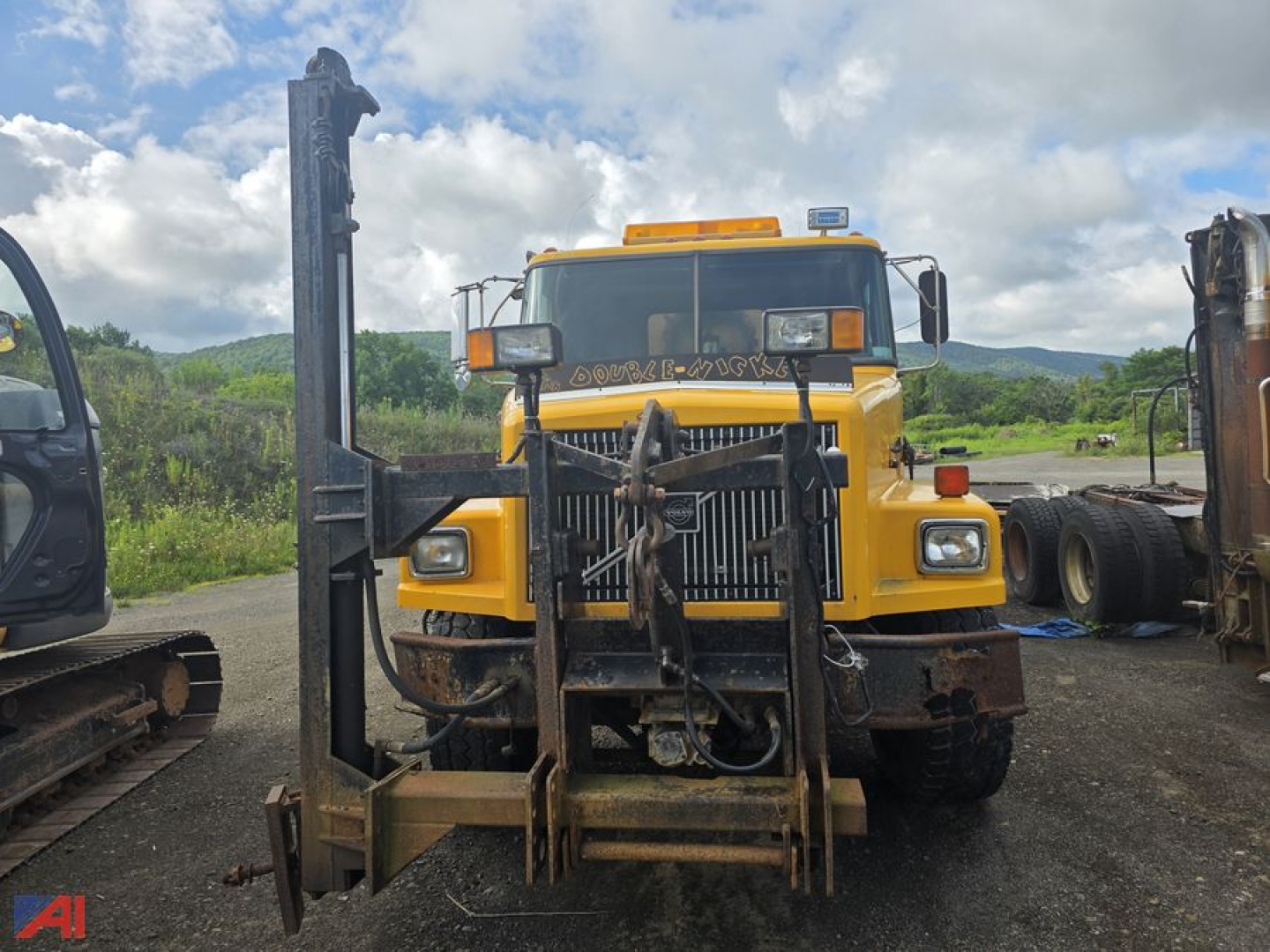 Front view of a yellow 1997 Volvo WG dump truck with a sander body, black heavy-duty fork lift setup on the front, grille, bumper, and orange beacon light on top.