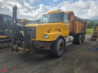 Volvo WG dump truck with sander body in yellow, front view showing snow plow mount and large grille, 6x4 configuration, worn front bumper and dump bed.