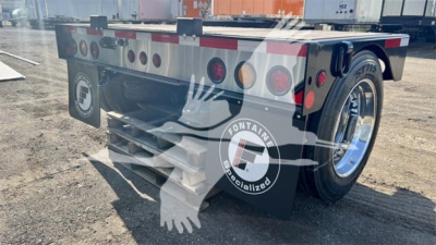 Fontaine flip axle trailer in rear three-quarter view showing dual axles, reflective tape, and round taillights. Visible text includes Fontaine Specialized logo on wheel cover and basic trailer frame details.