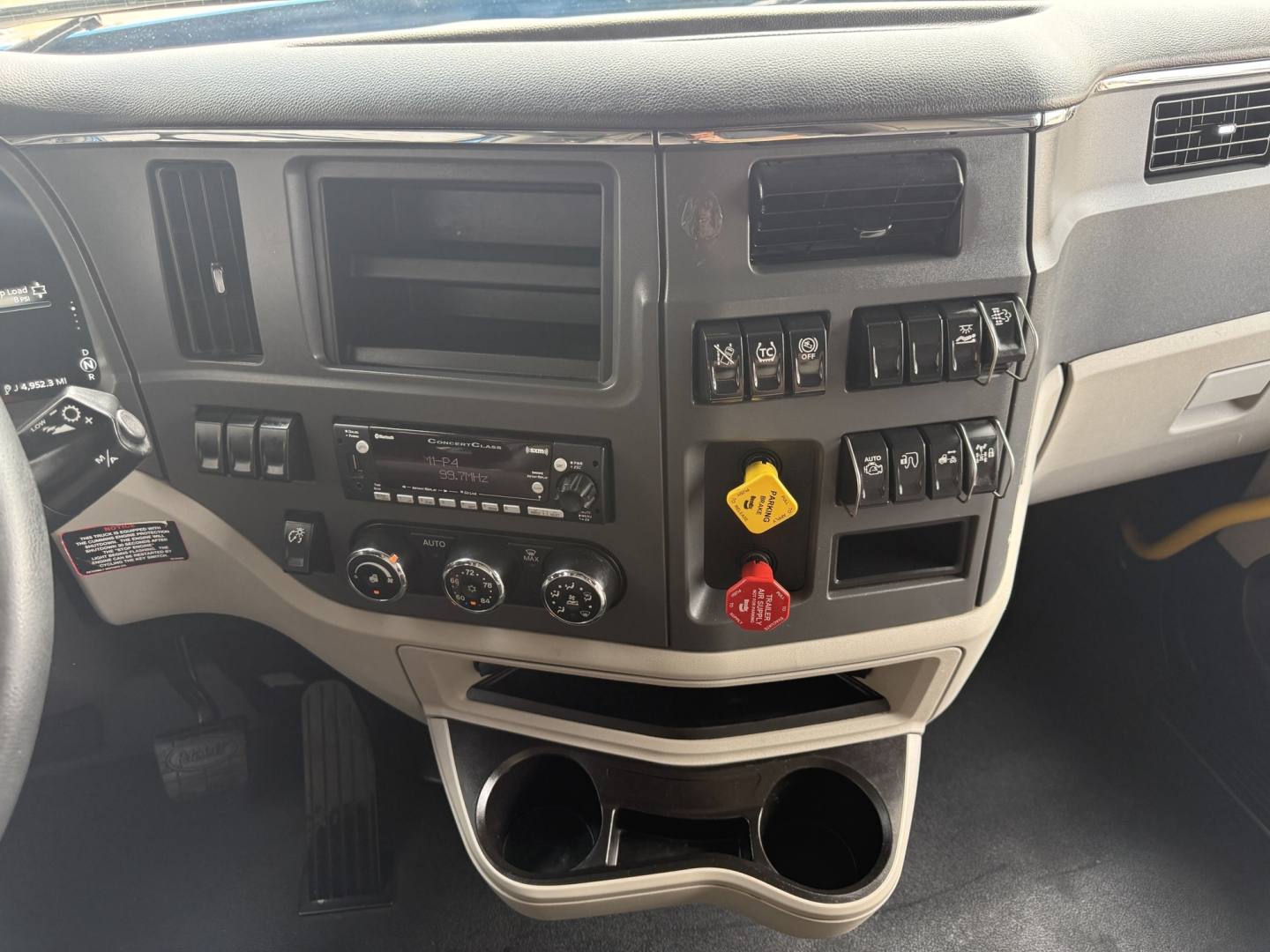 Cab interior dashboard of a Peterbilt 579 showing switch panel, empty radio slot, climate controls, and cup holders in lower dash.