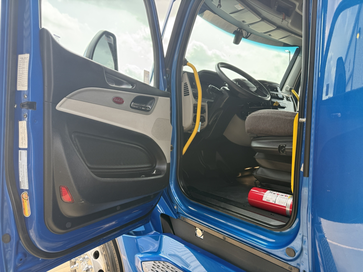 Peterbilt 579 truck cab interior with open door, blue exterior, steering wheel, driver seat, and dashboard.