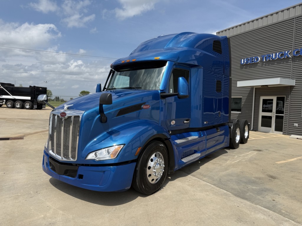 Peterbilt 579 tractor in blue, front-left view, parked outside a used truck lot.