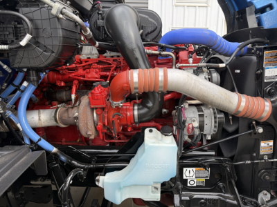 Peterbilt 579 engine bay with red engine block, blue hoses, black air intake, white coolant reservoir with 'RACOR' label visible, and orange exhaust pipe.