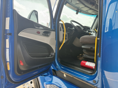 Peterbilt 579 truck cab interior with open door, blue exterior, steering wheel, driver seat, and dashboard.