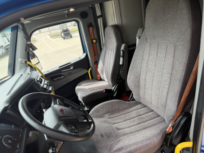 Interior of a 2022 Peterbilt 579 cab showing steering wheel, driver seat, passenger seat, dashboard, and door panel.