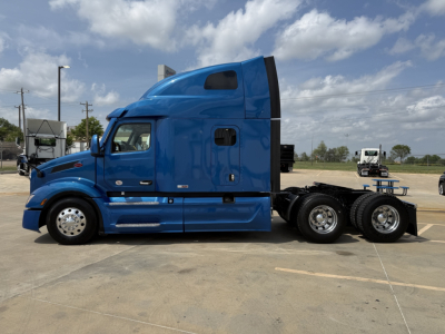 Peterbilt 579 truck side view showing blue cab and sleeper with two rear axles in a parking lot.