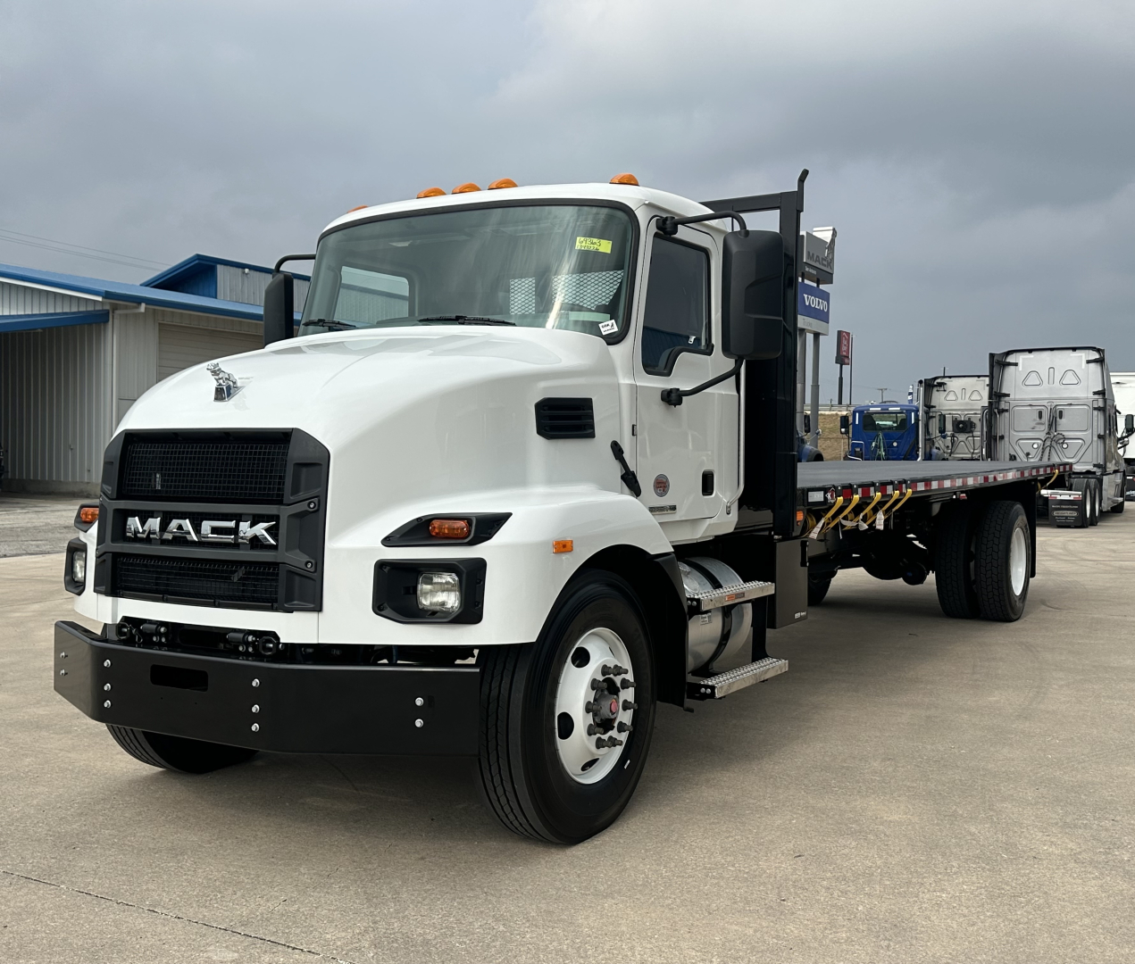 Mack MD6 flatbed truck in white, front-left view showing Mack grille, cab, and flatbed with yellow/black striped safety decals.