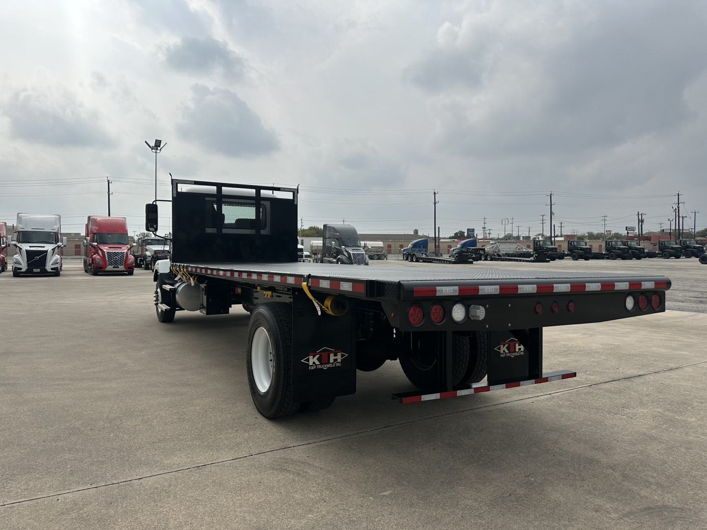 Flatbed truck rear view showing flatbed with black cab, rear dual wheels, and tail lights.
