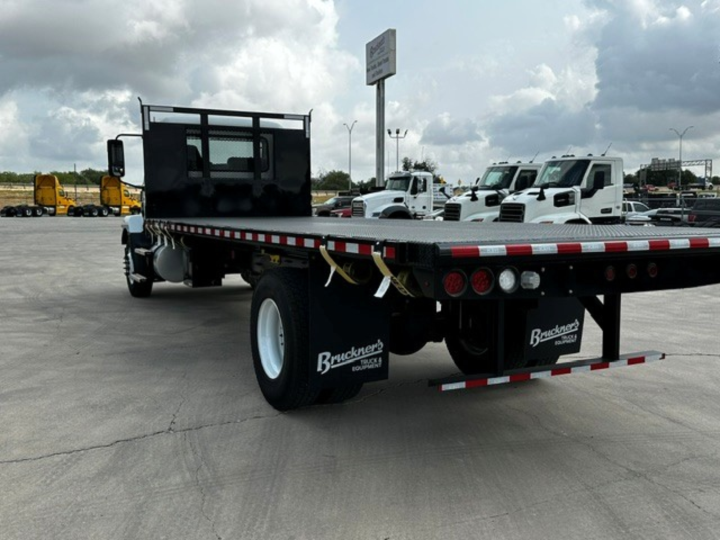 Mack MD6 flatbed truck rear view showing flatbed with dual rear wheels and Brackett-brand mudflaps.