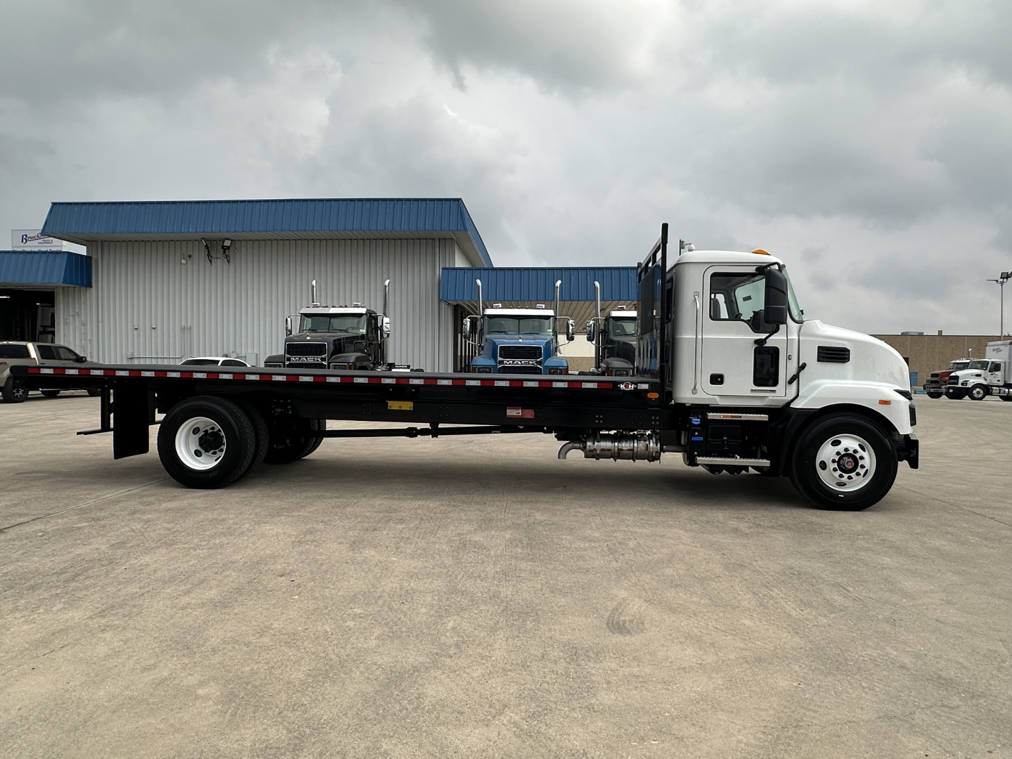 Flatbed truck in side view showing Mack MD6 with white cab and long black flatbed.