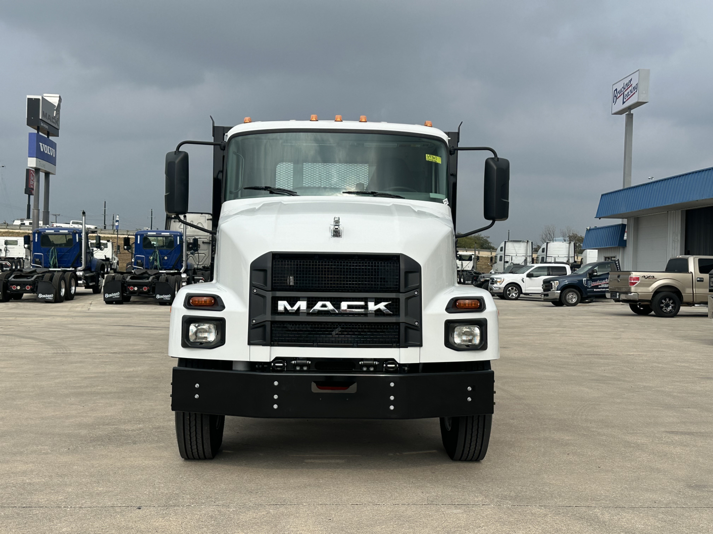 Front view of a white 2026 Mack MD6 flatbed truck showing bold grille with MACK logo, headlights, and bumper.