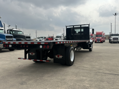 Flatbed truck trailer with empty bed, Mack MD6 not visible, multiple trucks in lot in background.