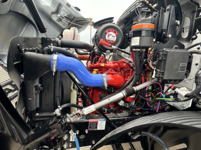 Mack MD6 engine bay showing blue coolant hose, red engine component, black radiator, and various hoses and wires.