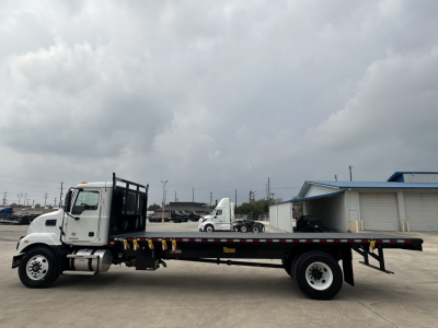 Flatbed tow truck in profile showing long black flatbed with dual rear wheels and white cab; No visible text on the truck exterior.