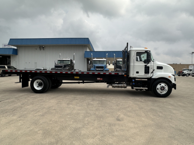 Flatbed truck in side view showing Mack MD6 with white cab and long black flatbed.