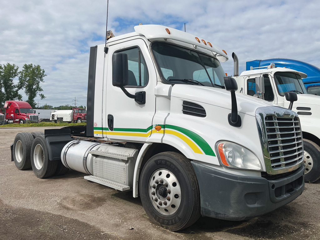  Freightliner Cascadia113 cab showing front grill and wheel, with green-yellow stripe on white truck.