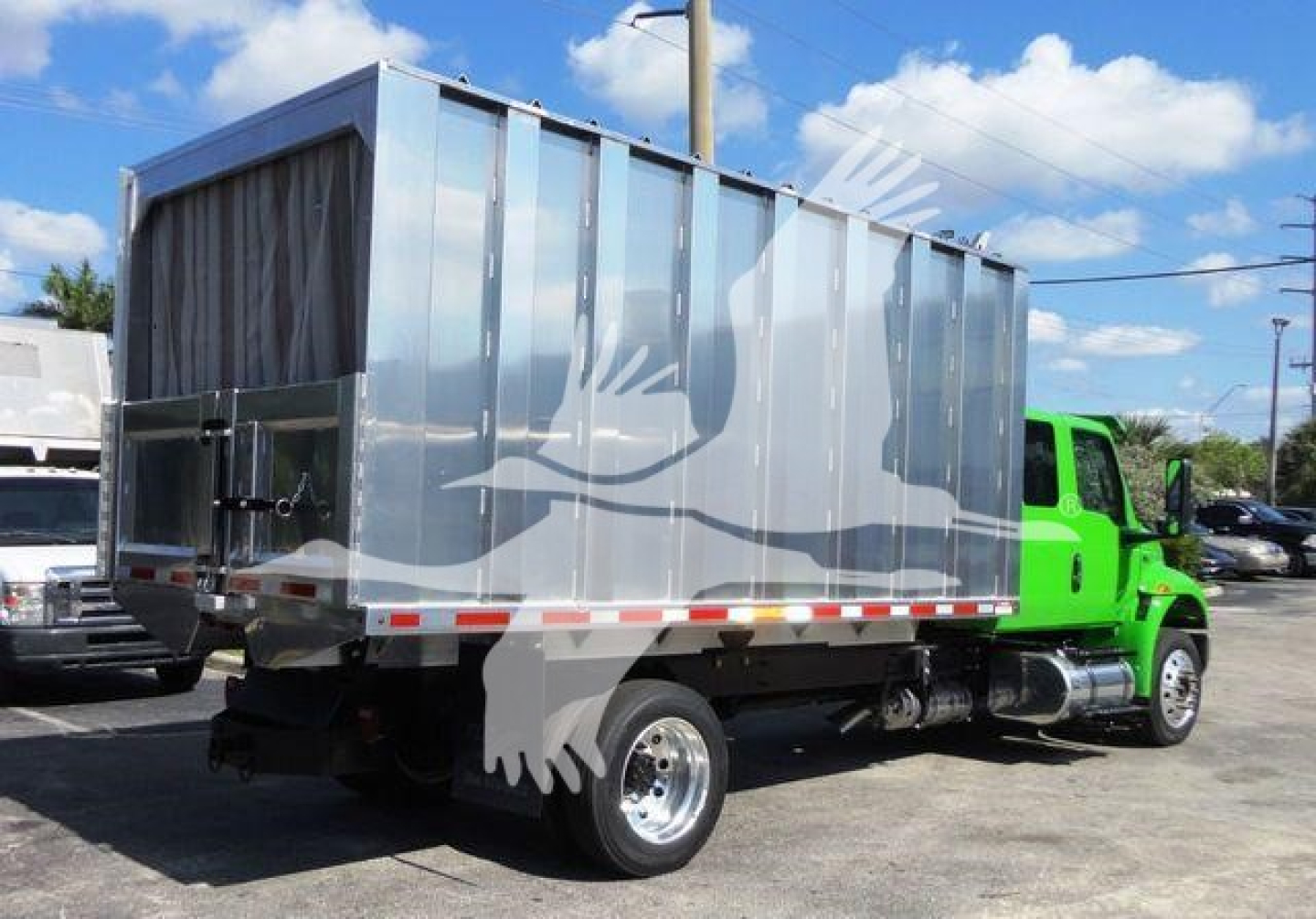 Truck cab and dump body on a medium-duty chassis showing silver box-style dump bed, green cab in background, side view with reflective stripes