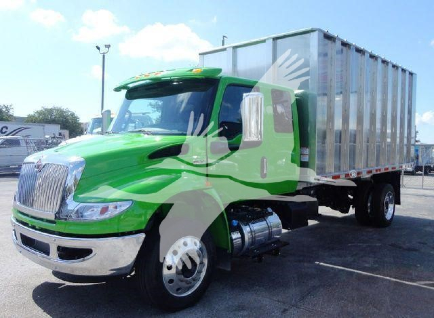 Truck with green cab and silver cargo box in a dealership lot, International MV model in the foreground.