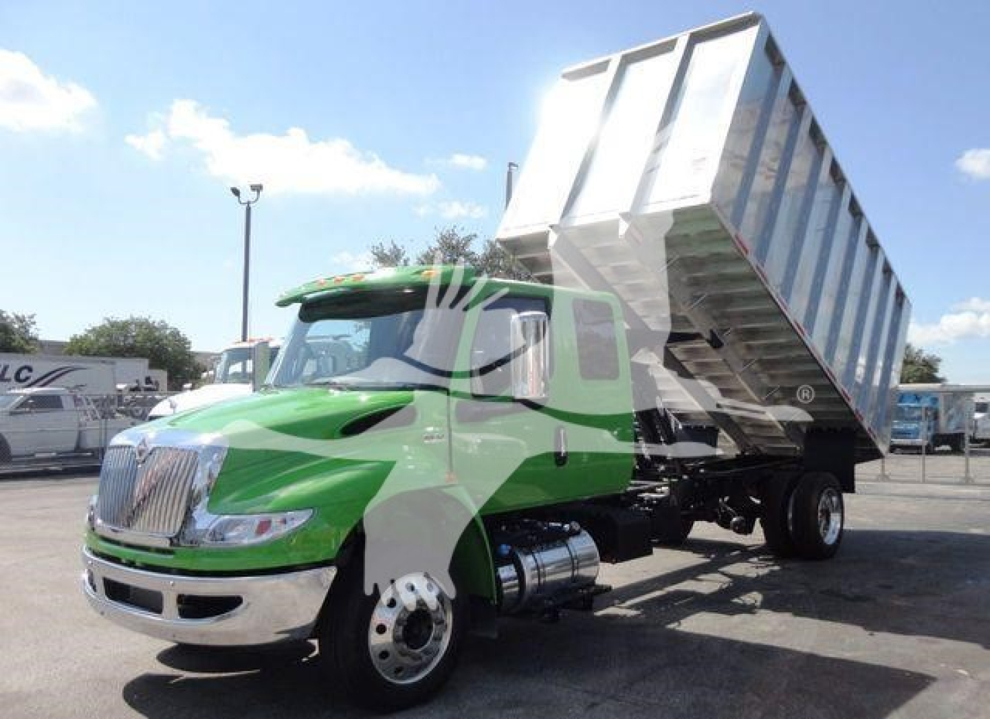 Green 2023 International MV dump truck with raised aluminum dump bed in a dealership lot.