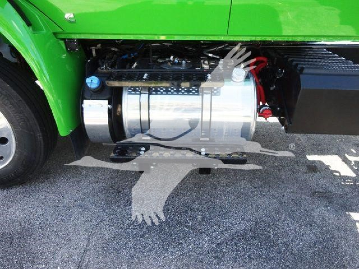 Truck fuel tank and side components on a bright green International MV chassis; metal cylindrical fuel tank with hoses and clamps visible.