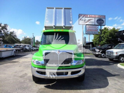 Front view of a bright green 2023 International MV dump truck in a dealership lot, with chrome grille, large silver dump bed, and surrounding trucks.