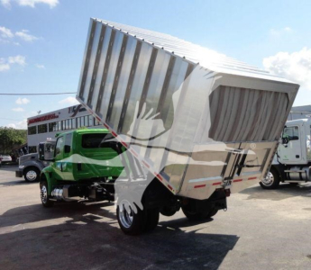 Truck mounted dump bed raising in a lot with other trucks visible