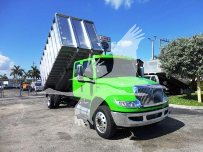 Green International MV chipper truck with raised dumping bed and dual rear wheels, front view showcasing cab and chrome grille.