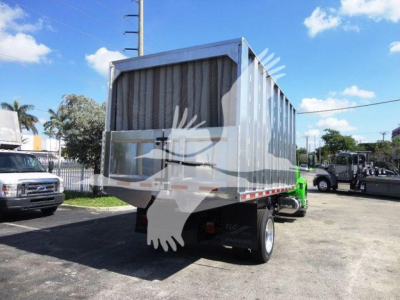 Truck dump trailer attached to green chassis in a dealership lot. Large open-top metal hopper with vertical ribs and tailgate. Side railing and rear lighting visible.
