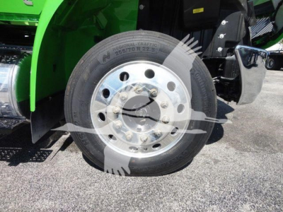 Front wheel of a green International MV truck showing a large silver steel rim and tire with visible lug nuts and part of the front fender.