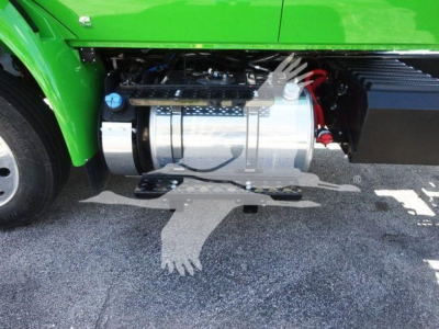 Truck fuel tank and side components on a bright green International MV chassis; metal cylindrical fuel tank with hoses and clamps visible.