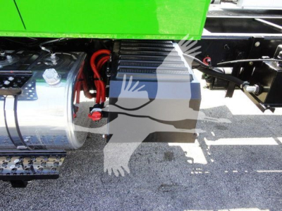 Truck undercarriage showing chrome fuel tank, red battery cables, and black side step with ribbed steps. Green chassis visible with a silver cylindrical component and wiring.