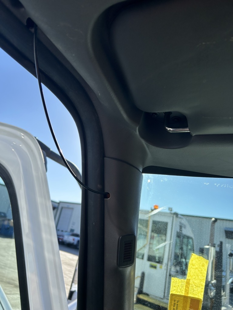 Cab interior A-pillar view of a 2020 International MV truck with sun visor and window; exterior lot with other trucks visible through the windshield.