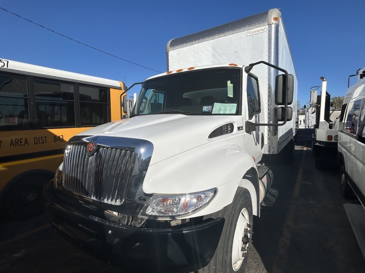 Truck cab and box truck in a lot showing International MV with chrome grille and white body, side mirror, and attached box trailer.