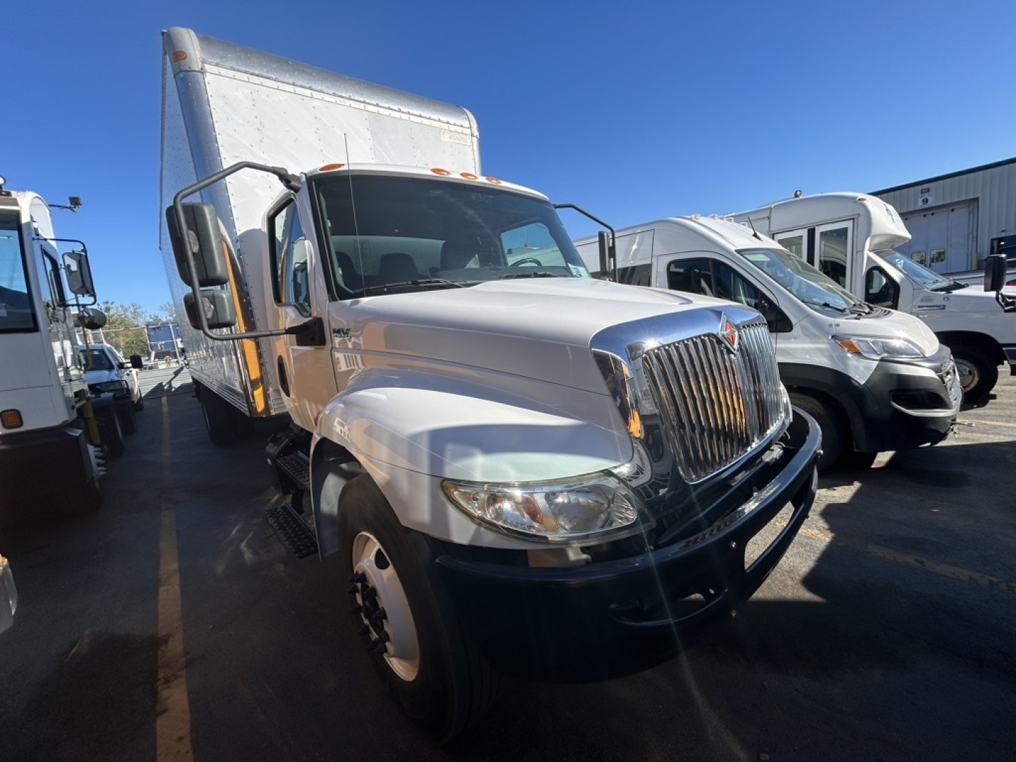 Truck front-left view of a 2020 International MV box truck showing front grille with chrome, large side mirrors, and white cargo box.