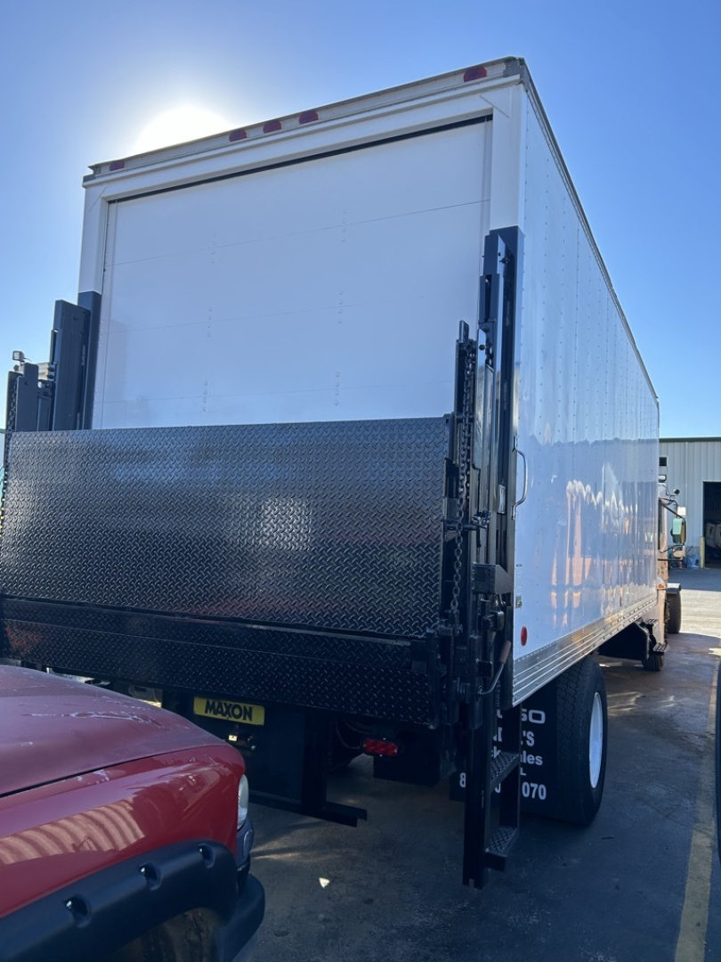 Box truck rear view showing lift gate and diamond plate ramp with white cargo box and black undercarriage.