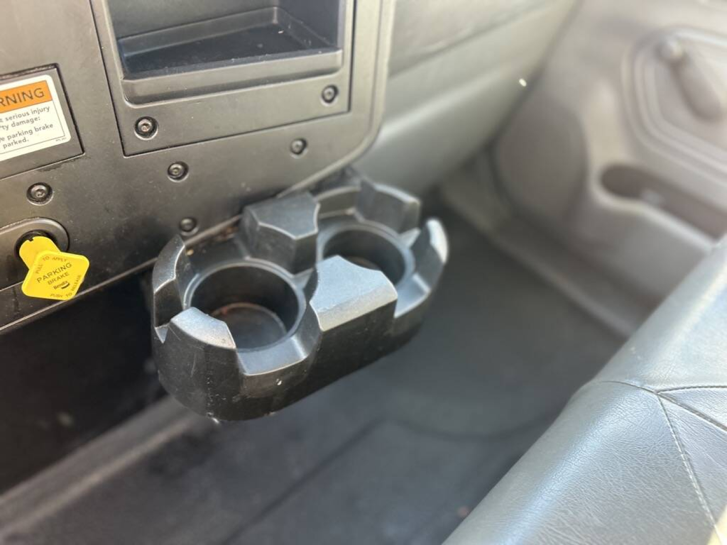 Cup holder with two circular slots and a central divider in the truck cab, mounted below a dashboard panel with a yellow ignition/lock knob nearby.