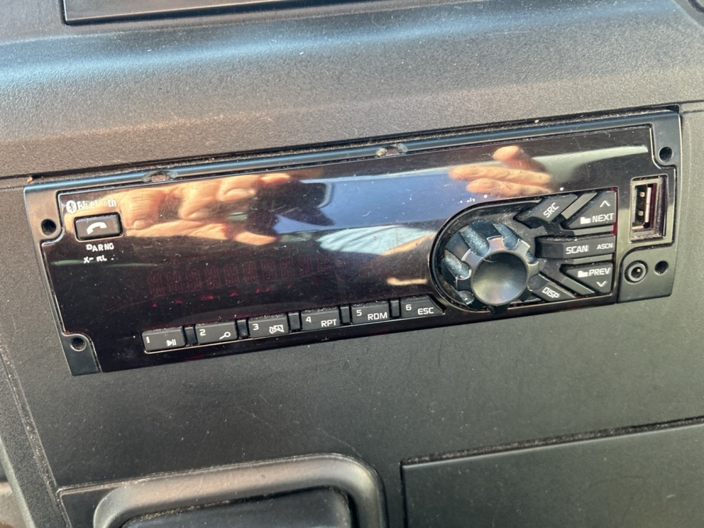 Dashboard stereo head unit in a truck cab showing a single-DIN car radio with rotary volume knob and buttons labeled, blank bezel surrounding unit.