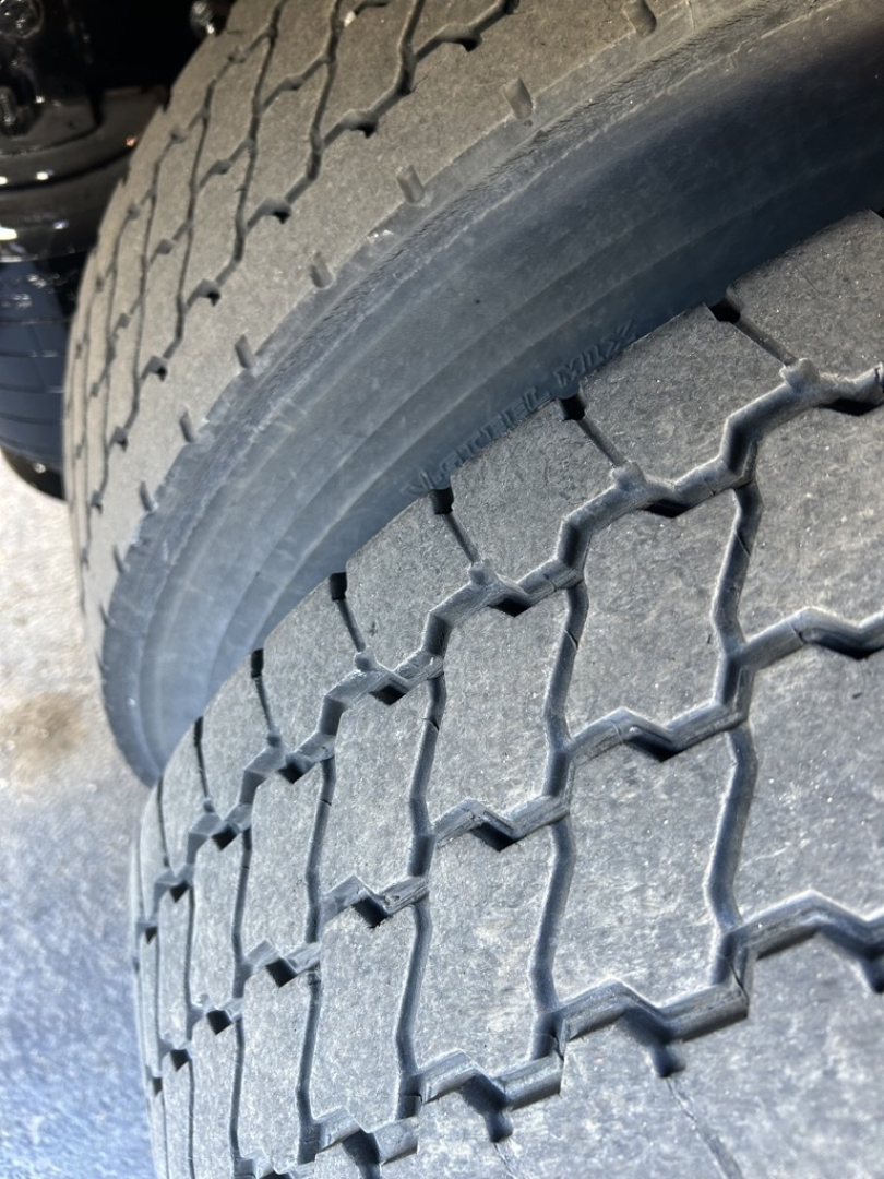 Tire tread close-up on a commercial box truck, showing a rugged zigzag tread pattern and part of the wheel well.