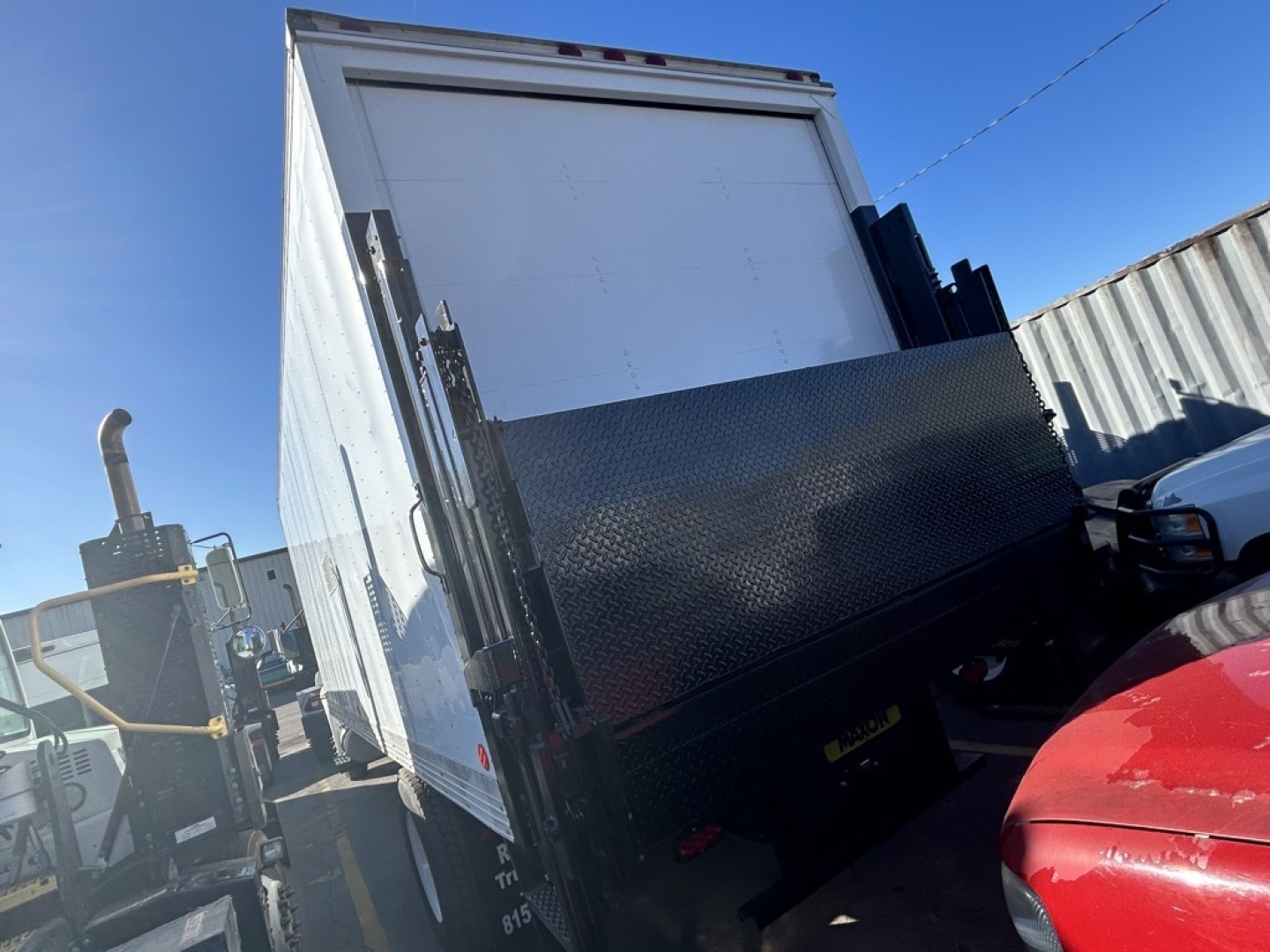 Truck box rear view showing diamond plate steel lower panel and raised cargo area of a box truck, part of a hitch and wheel visible