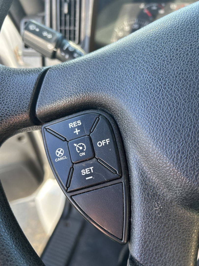Steering wheel close-up with cruise control buttons visible on left, including RES+/SET-, CANCEL, ON/OFF, and cruise switch cluster.