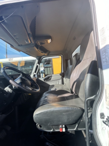 Truck cab interior showing front bench seat and driver area of a 2020 International MV, with steering wheel, dashboard, and door frame.