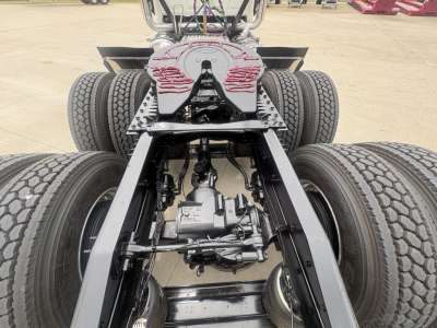 Rear chassis of a new Mack PI64T daycab showing drive axles, differential, suspension, and dual rear tires with visible battery wiring.