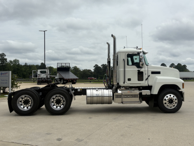 Mack PI64T conventional daycab truck side view showing exhaust stacks, fuel tanks, and dual rear axles.
