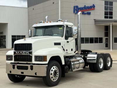Mack PI64T truck in white, front and side view showing dual rear axles, chrome bumper, and Mack grille; dealership building in background.