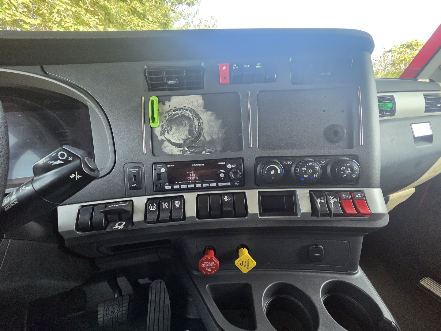 Kennworth T680 dash area showing control panel and dashboard switches with labels and gauge cluster; visible text includes various dials, warning icons, and a small radio display.