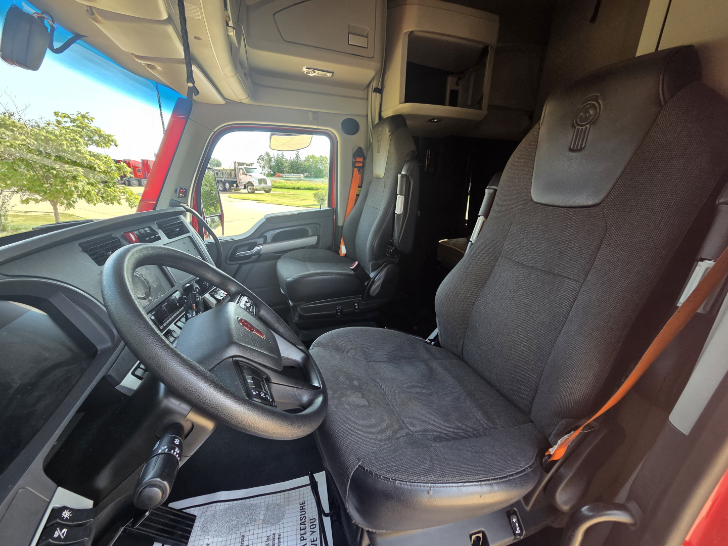 Interior of a Kenworth T680 truck cab with dual front seats, dashboard, steering wheel, and driver’s seat clearly visible.